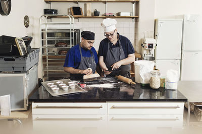 Young man showing digital tablet to coworker while cooking in kitchen