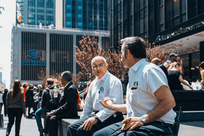 People sitting on street against buildings in city