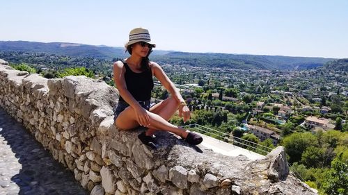 Young woman sitting on retaining wall against townscape