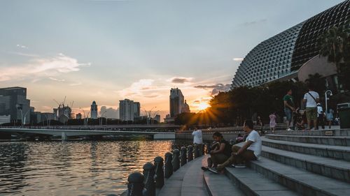 People sitting on bridge over cityscape against sky during sunset