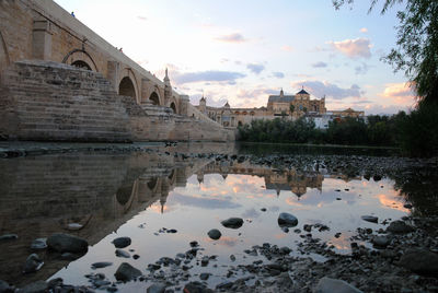 Mosque of cordoba and its reflection next to the roman bridge on the guadalquivir river at dusk