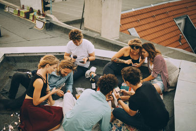 High angle view of distracted friends using mobile phones while partying on rooftop