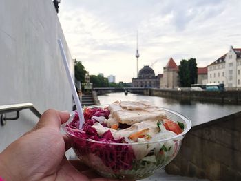 Cropped hand holding food in container by spree river in city