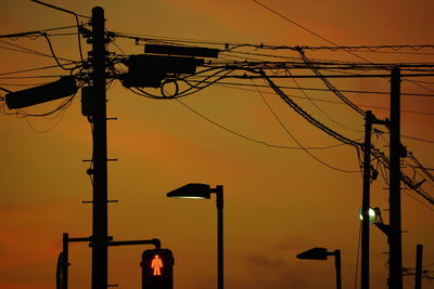 Low angle view of electricity pylon against orange sky
