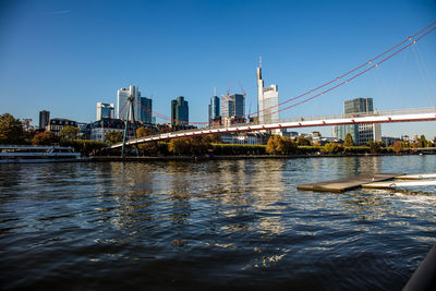 Bridge over river by buildings against clear blue sky