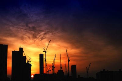 Silhouette of factory against sky during sunset