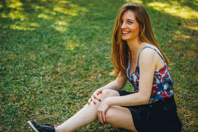 Beautiful smiling young woman sitting on grass at park