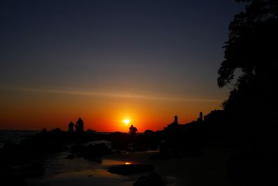 Silhouette trees by sea against sky during sunset