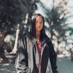 Portrait of young woman standing against trees