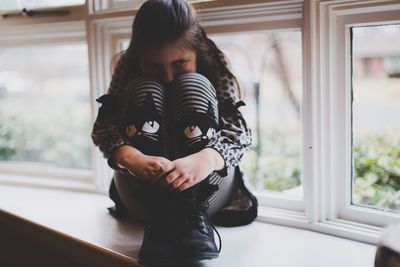 Full length of girl sitting on window sill at home