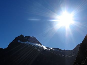 Low angle view of snowcapped mountains against blue sky on sunny day