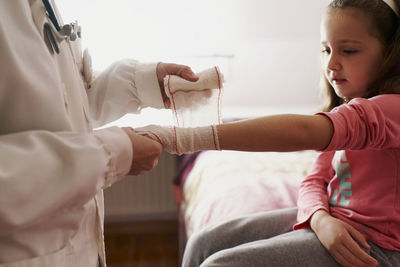 Female doctor bandaging the arm of a little girl in her room. home doctor concept