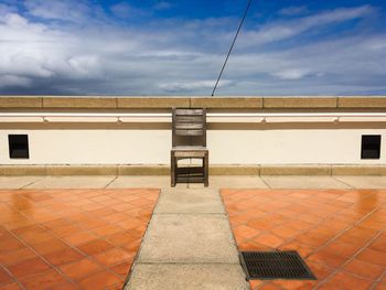 Empty chair in building terrace against sky