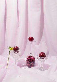 Still life arrangement of cristal glasses filled with red plums against light violet background. 