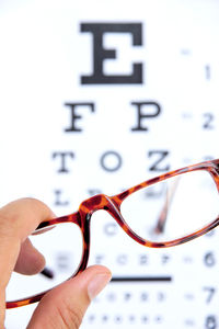 Cropped hand holding eyeglasses against eye chart