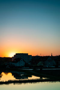 Reflection of houses and buildings against clear sky during sunset