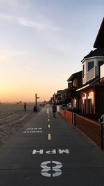 City street by buildings against sky during sunset