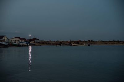 Illuminated buildings by sea against clear sky at night