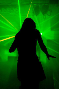 Silhouette woman dancing against illuminated light at night