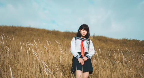 Portrait of young woman standing on field against sky