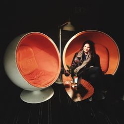 Young woman sitting against black background