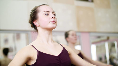 In dancing hall, young ballerina in purple leotard performs a certain ballet exercise