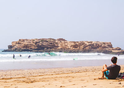 People sitting on beach by sea against clear sky