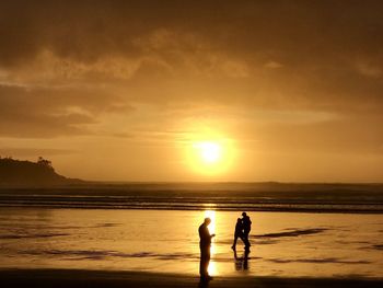 Silhouette people on beach against sky during sunset