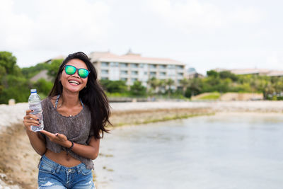 Smiling young woman holding water bottle while walking at riverbank