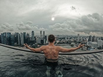 Rear view of shirtless man in swimming pool against buildings in city
