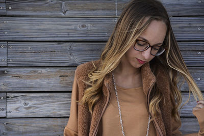 Young woman looking away while standing against wooden wall