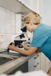 Blond female veterinarian examining blood test under microscope at medical clinic