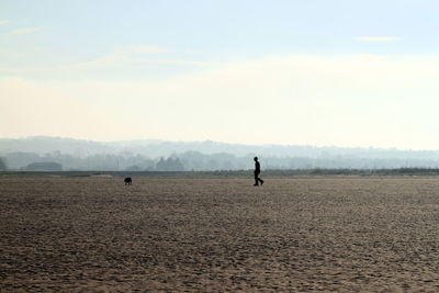 Person with dog on arid field against cloudy sky