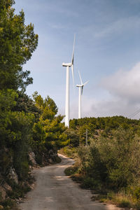 Path leading towards windmills against cloudy sky