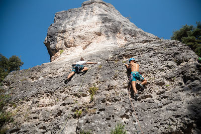 Low angle view of man and woman rock climbing in forest