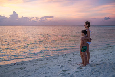 Rear view of woman standing at beach against sky during sunset