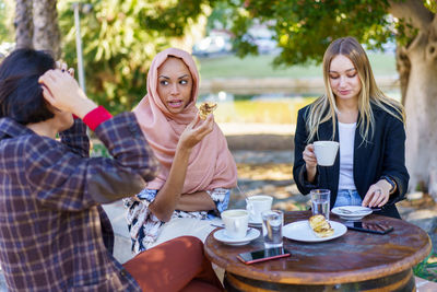 Portrait of smiling friends using smart phone while sitting on table