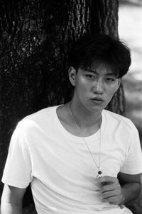 Portrait of young man looking away against tree trunk