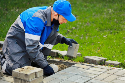 Bricklayer in work clothes sits on sidewalk and lays out paving slabs. sight of working man in open