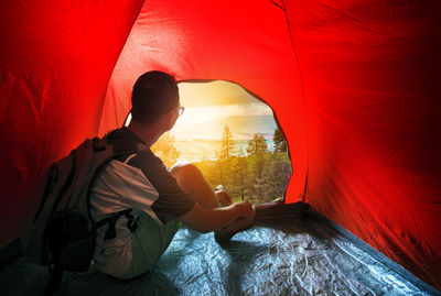 Rear view of man sitting on red wall against orange sky