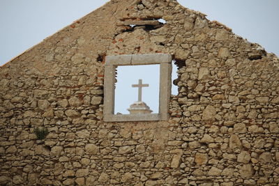 Low angle view of cross on old building against sky