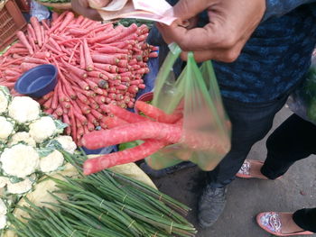 Close-up of man holding paper currency and carrots in plastic bag at market