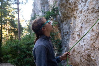 Side view of hiker holding rope while standing by rock