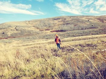 Rear view of woman with gun walking on mountains against sky