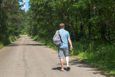 An adult male traveler with a backpack is walking alone empty road in the middle forest.