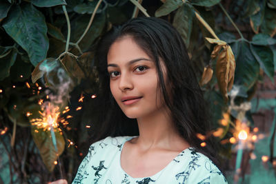 Portrait of girl holding illuminated sparklers against plants