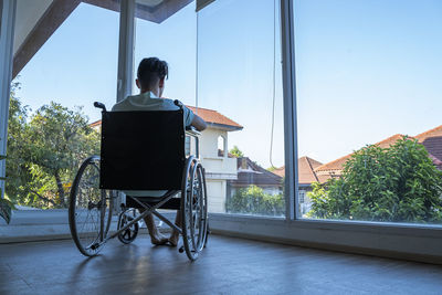 Rear view of man sitting on window