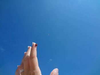 Low angle view of hand against blue sky