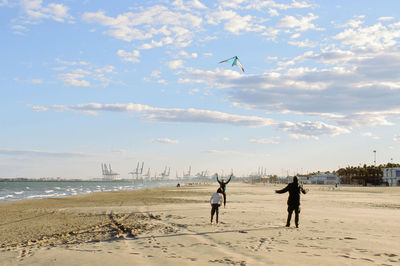 People flying kite at beach against sky