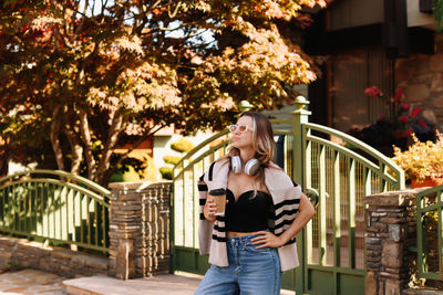 Portrait of young woman using mobile phone while standing against trees